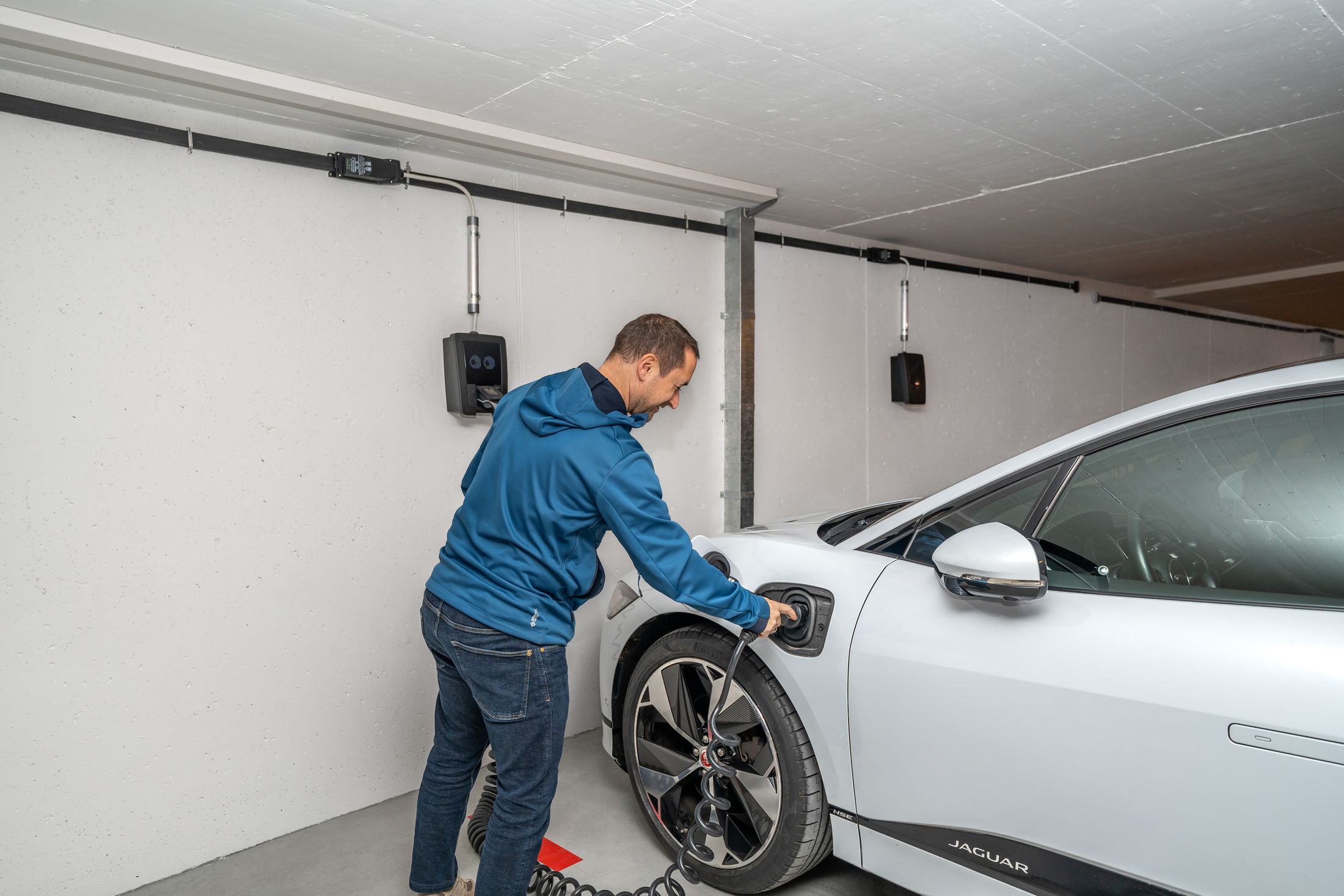 Man plugging a wall-mounted home charger into a white electric SUV in his garage