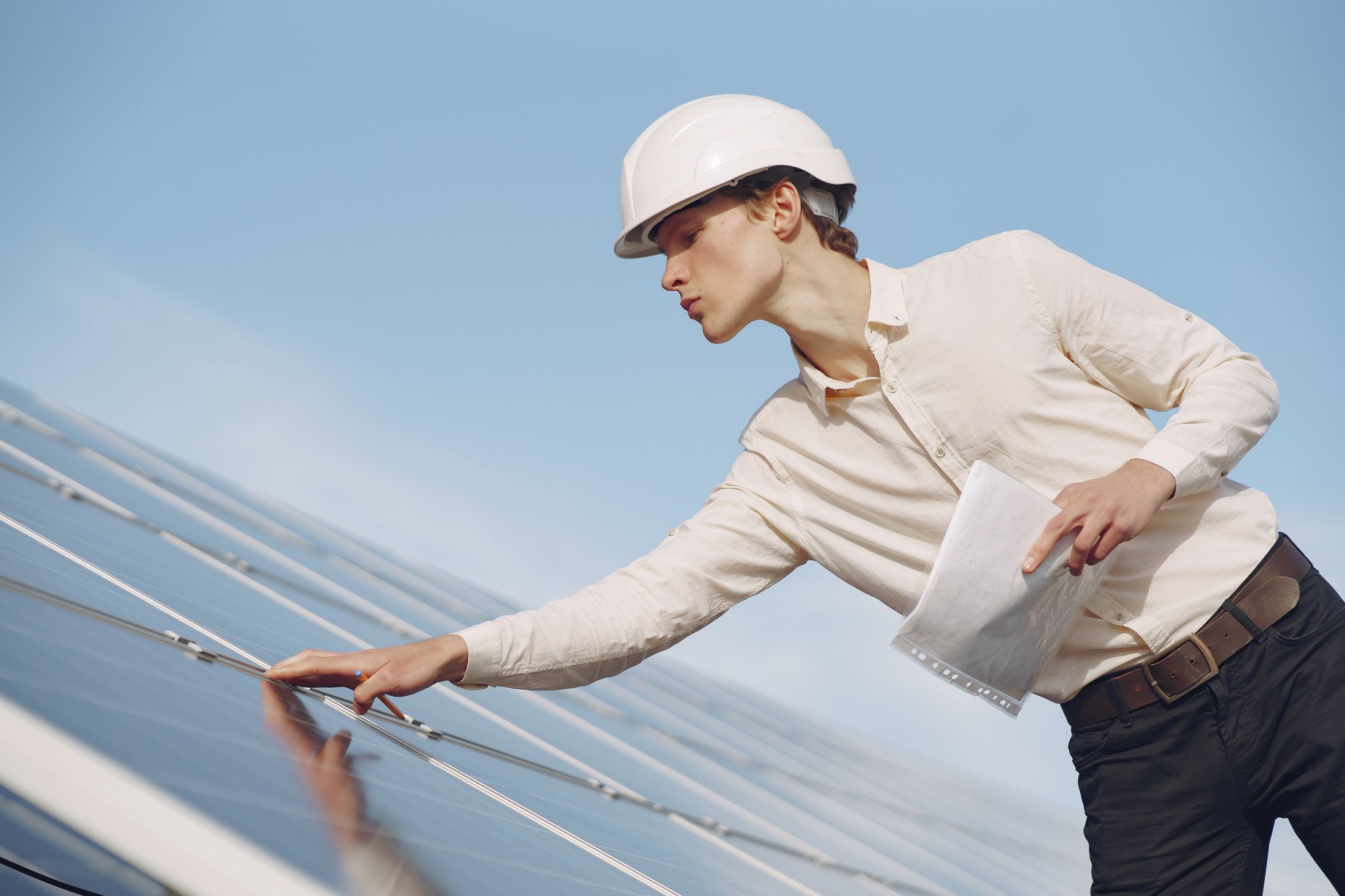 Technician in a hard hat running a hand across solar panels during a rooftop inspection